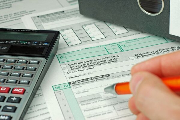 Hand mit Kugelschreiber ist dabei zu sehen, wie sie ein Formular für die Einkommensteuererklärung ausfüllt.